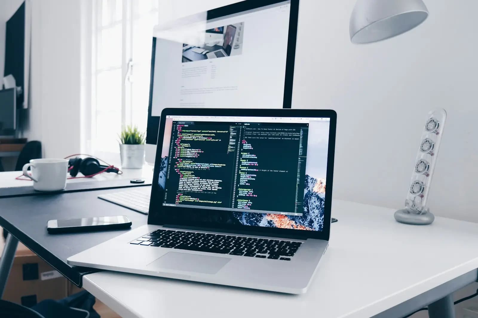A MacBook with lines of code on its screen on a busy desk — illustrating Designing WordPress plugins people trust.